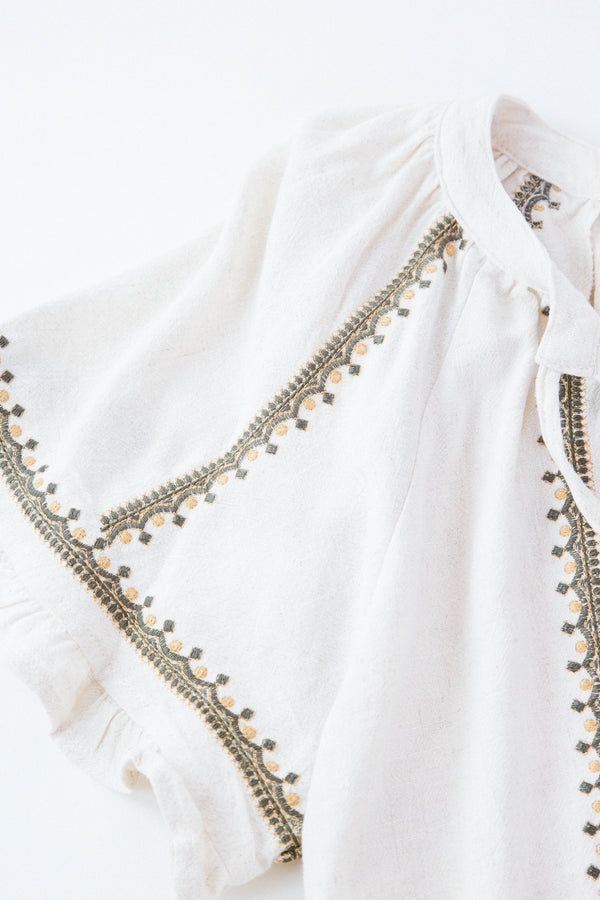 Detail shot of embroidered cream shirt on white background