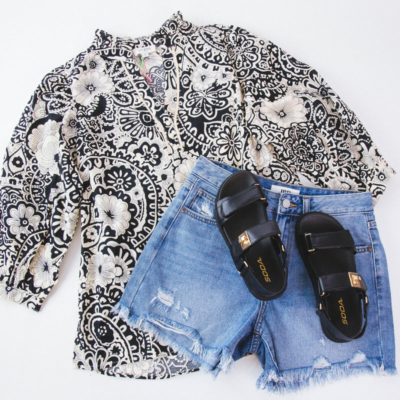 Black and white paisley 3/4 sleeve top on a white background with denim shorts and black sandals