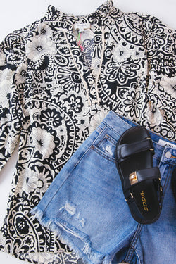 Black and white paisley 3/4 sleeve top on a white background with denim shorts and black sandals