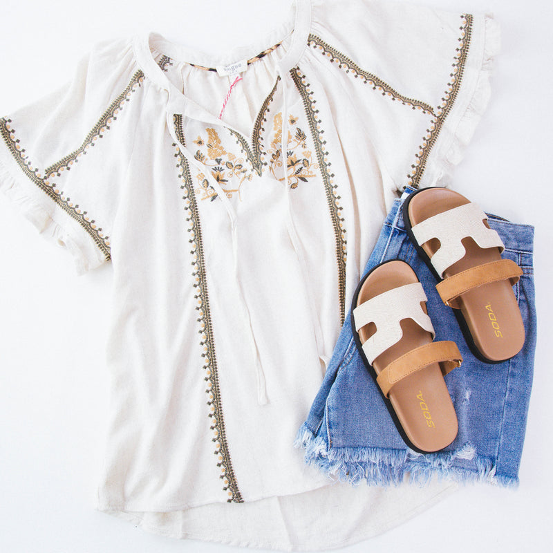 Cream embroidered shirt on a white background with denim shorts and neutral sandals